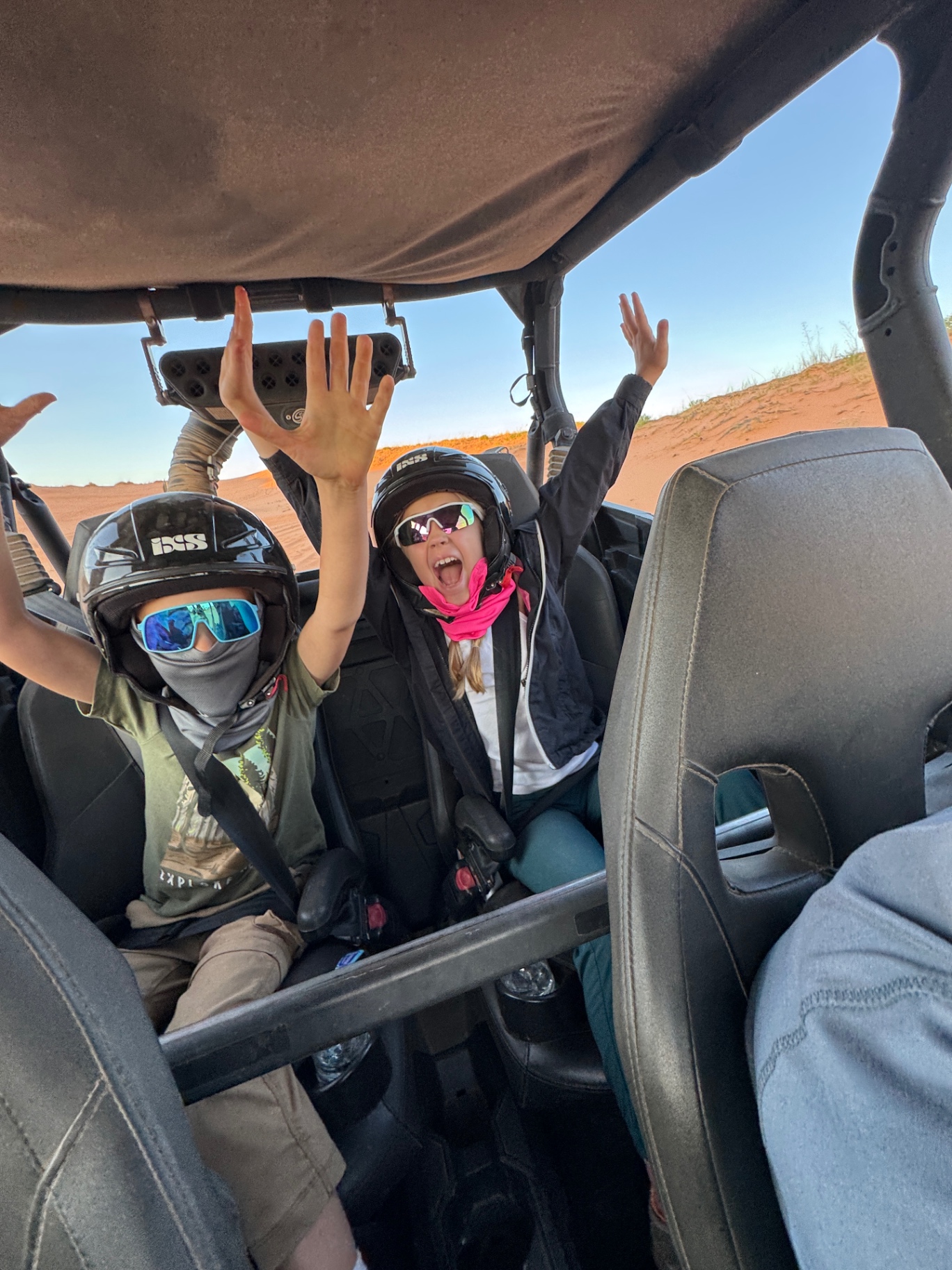 The Venture Seekers kids in helmets and face coverings in a UTV at Coral Pink Sand Dunes in Southern Utah at golden hour